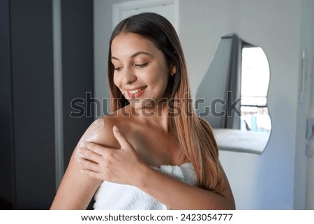 Portrait of gorgeous young woman with long hair applying body cream on her shoulder. Body lotion, moisturizing cream, sun protection cosmetics concept. Royalty-Free Stock Photo #2423054777