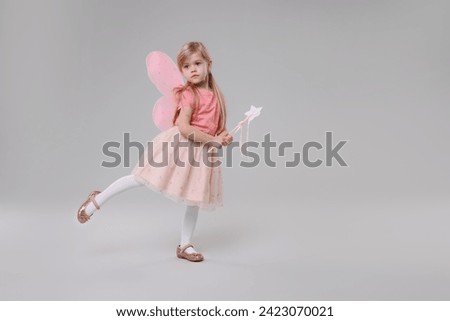 Cute little girl in fairy costume with pink wings and magic wand on light grey background, space for text