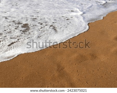 wave of foamy sea water on golden sand, background of beach detail
