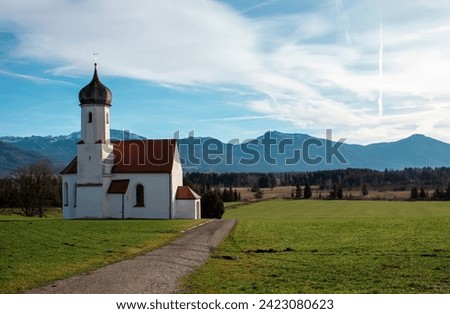 Idyllic landscape, church against the backdrop of the Alps mountains with mountain chalets and green fields.