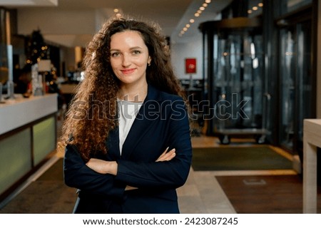 smiling curly female employee stands in the hotel lobby staff manager receptionist hospitality Royalty-Free Stock Photo #2423087245