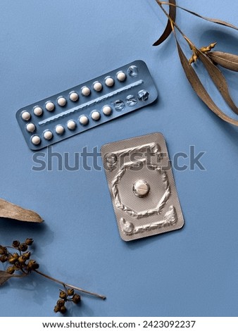 Two different packs of contraceptive pills on colored paper background with eucalyptus leaves, overhead view. Monthly pack and a morning-after pill, illustrating concept of modern female health. Royalty-Free Stock Photo #2423092237