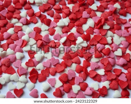 Colored sugar sprinkles in the shape of cute hearts are scattered on a light background. Close up