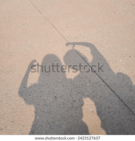 Shadow silhouette of two girls trying to make heart sign with hands