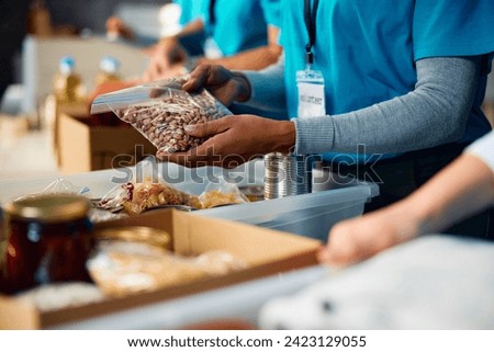 Close up of volunteer packing donated food into cardboard boxes at community center. Royalty-Free Stock Photo #2423129055