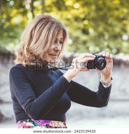 caucasian 70s senior fit happy lady relax with photo camera in park wear floral skirt and black long sleeve shirt