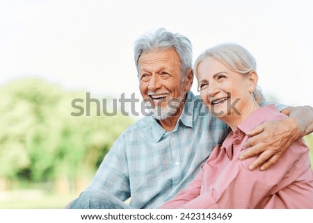 Happy active senior couple having fun talking and hugging sitting on a bench in park outdoors Royalty-Free Stock Photo #2423143469
