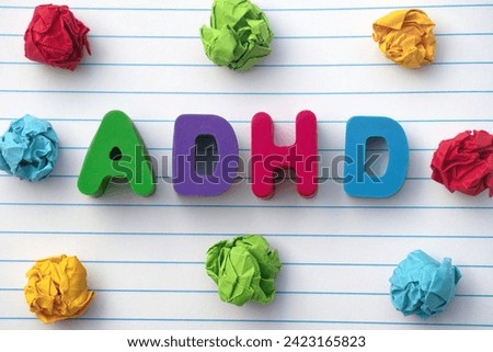 ADHD. The abbreviation ADHD on a notebook sheet with some colorful crumpled paper balls around it. Close up. ADHD stands for Attention deficit hyperactivity disorder.