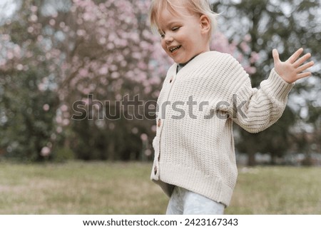 Cute blonde girl having fun in the park near a blooming magnolia