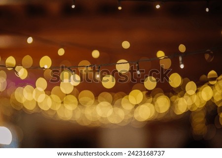 Valmiera, Latvia - July 7, 2023 - Focused string lights with blurred golden bokeh effect against a dark backdrop. Royalty-Free Stock Photo #2423168737