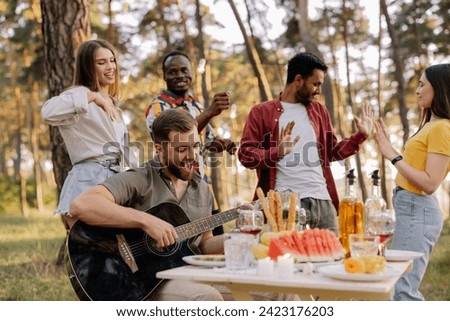 Multicultural group of people, bearded hipster man playing guitar and friends dancing and having fun