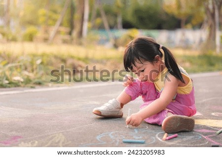 Asian girl three year old sitting on the asphalt pavement drawing with chalk in park in day childhood on summer sunny day, Creative development of children