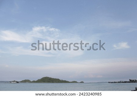 a green island in the middle of a blue sea, with a clear blue sky and thin clouds