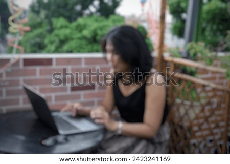 blurred image of a woman is working on a laptop in a rooftop cafe