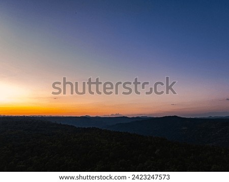 Aerial view A breathtaking sunset paints the sky with vibrant hues of orange and red, 
casting a warm glow over the majestic mountains in a tranquil evening landscape
