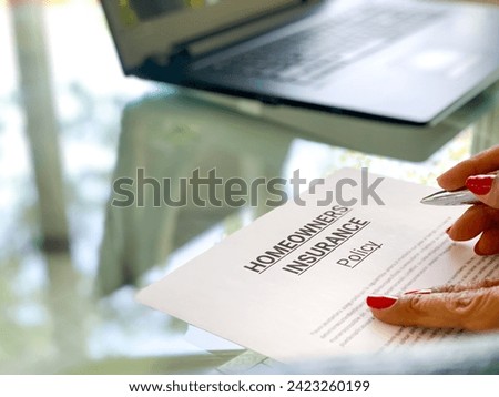 Woman's hands following a paragraph of a Homeowners Insurance Policy form while reading it before signing it and a  laptop in the background for real estate concept