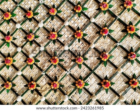 In the picture, there is a flower arrangement made from yellow corn seeds and dark pink amaranth flowers in the center, like a beautiful cherry blossom, in a long bamboo woven wall, very beauti