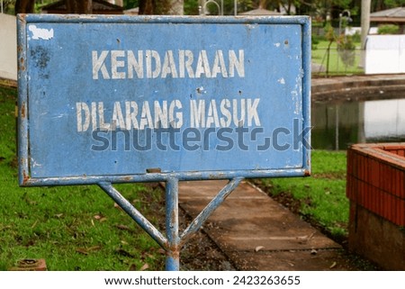 A prohibition notice board with a blue background reading "VEHICLES ARE NOT ENTERED" in white, in the garden yard of the housing complex.