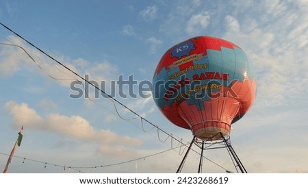 A replica of a hot air balloon in the recreation area used to take pictures of visitors, reading "Welcome to Kuala Gunung Rice Field Tour", was taken from below against the backdrop of the sky.