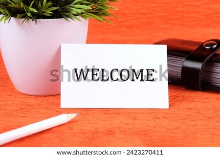 Business Concept. Welcome text written on a business card next to a business card holder, a green flower and a pencil on an orange background