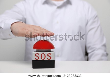 Man pressing red SOS button at white table, closeup