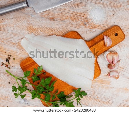 Raw fish with condiments, halibut fillet with garlic and parsley on wooden table