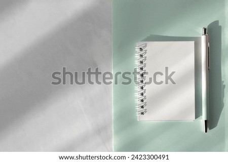 Minimalist aesthetic feminine home office workspace, blank notebook mockup, pastel sage green paper stationery, pen on gray marble neutral desktop background with natural sun light shadows.