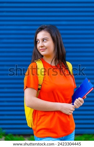 Vertical photo of a cute student with casual colorful clothes and textbooks standing outdoors