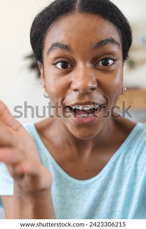 Excited young biracial woman gestures animatedly at home on video call. Her lively expression adds a personal touch to the cozy indoor setting.