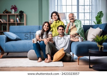 Cheerful Indian family having tea or coffee together at home looking at camera Royalty-Free Stock Photo #2423323057