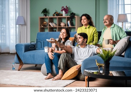 Indian family of four on sofa, engrossed in watching TV, switching channels with remote