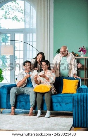 Cheerful Indian family having fun while using smartphone at home Royalty-Free Stock Photo #2423323433