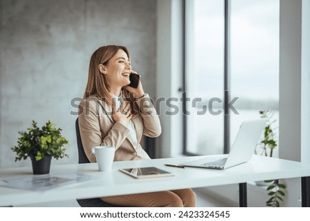 Young business woman on the phone at office. Business woman texting on the phone and working on laptop. Pretty young business woman sitting on workplace. Smiling business woman.