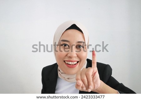 Portrait of excited Asian woman wearing hijab showing the little finger dipped in purple ink after the voting for general election or Pemilu for the president and government of Indonesia.
