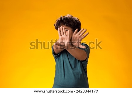 Portrait of child boy showing stop gesture on yellow background. Bulling and negative emotions concept
