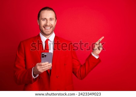 Photo portrait of handsome young guy point empty space hold gadget dressed stylish classic outfit isolated on red color background