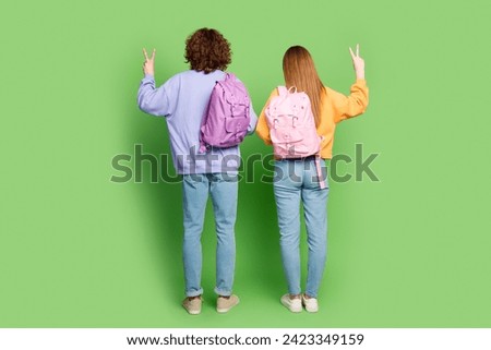 Full body rear behind photo of two people carry backpack demonstrate v-sign isolated on green color background