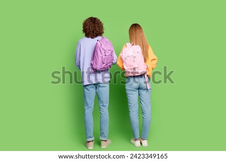 Full length rear behind photo of two young people carry backpack isolated on green color background