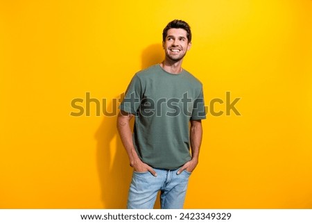 Portrait of pleasant positive guy wear stylish t-shirt plams in pockets look at promo empty space isolated on yellow color background