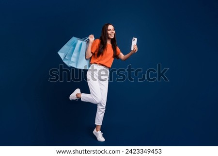 Full length photo of positive funky woman dressed orange t-shirt rising shoppers vlogging modern gadget isolated dark blue color background