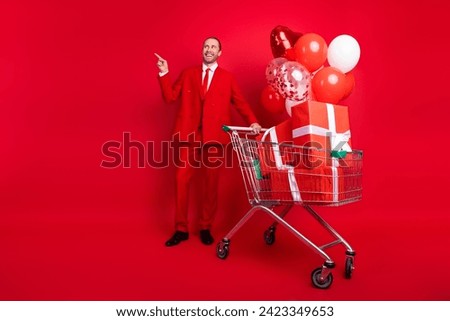 Full body photo of attractive young man point empty space gifts balloons dressed stylish classic clothes isolated on red color background