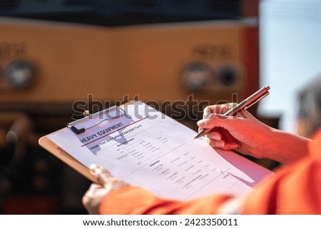 A service technician is checking on heavy machine maintenance checklist, with an ancient train locomotive head as blurred background. Transportation industrial working scene, selective focus at hand.