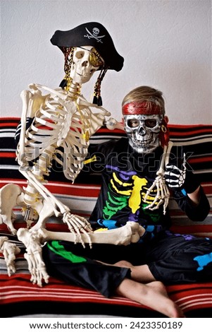 Young boy 7- 9 year old dressed as a colourful skeleton sitting on the sofa with the pirate skeleton