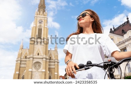 Female tourist with bicycle standing on town square in front of Name of Mary Church in Novi Sad Serbia and looking at attractions.