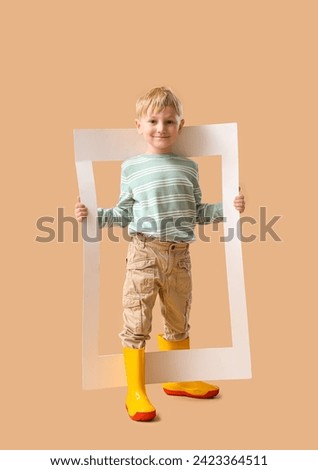 Little boy in rubber boots with frame on beige background