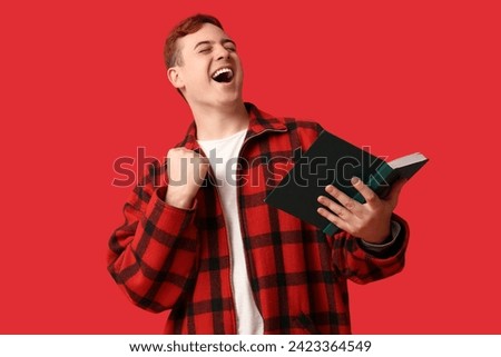 Happy young man with book on red background