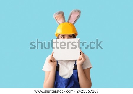 Female worker in bunny ears with blank card on blue background. Easter celebration