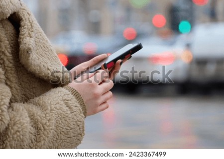 Female hands with smartphone close up on blurred lights background. Woman using mobile phone on a city street in winter