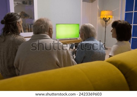 Family watching TV. Green screen. A young man, grandparents and a mature woman are sitting on the sofa and watching TV. Grandfather presses a button on the TV remote control.