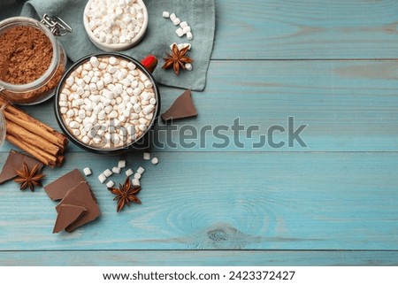 Tasty hot chocolate with marshmallows and ingredients on light blue wooden table, flat lay. Space for text